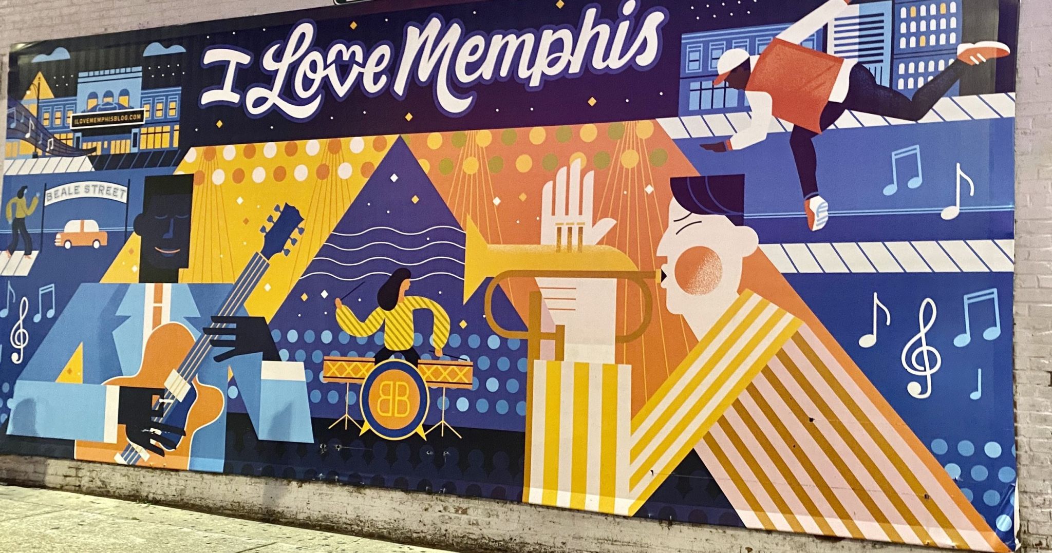 Shows a colorful mural with the text “I Love Memphis” at the top. The artwork features stylized illustrations of musicians playing guitar, trumpet, and drums, as well as a dancer performing a handstand. Iconic Memphis imagery is present, including the Beale Street sign, musical notes, and bright, geometric patterns in shades of blue, yellow, and orange.