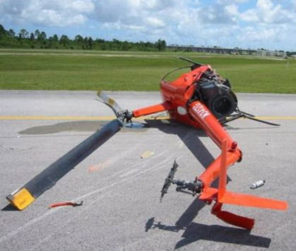 helicopter crashed on its side, on a runway with two men standing by it taking notes